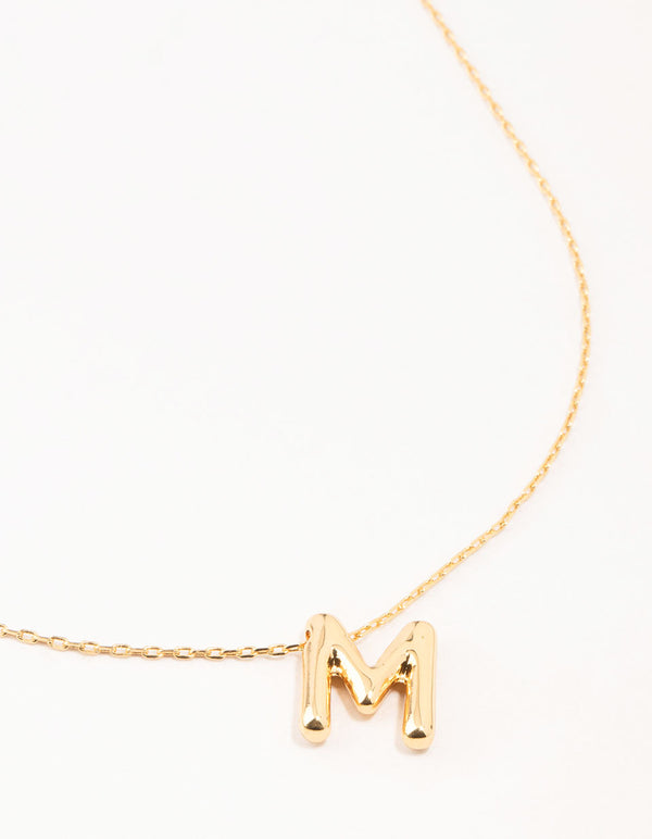 Showcasing a bubble letter M necklace with initials in gold plated finish close up view