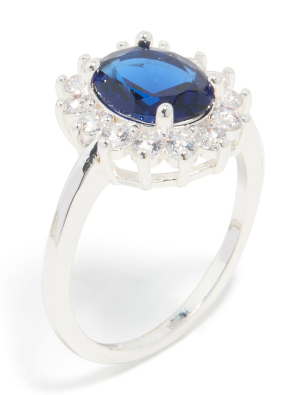 Highlighting a statement ring with oval cut blue cubic zirconia center stone surrounded by crystal border in plated metal side detail view