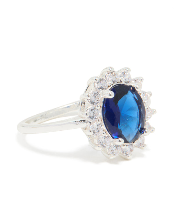 Highlighting a statement ring with oval cut blue cubic zirconia center stone surrounded by crystal border in plated metal side detail view