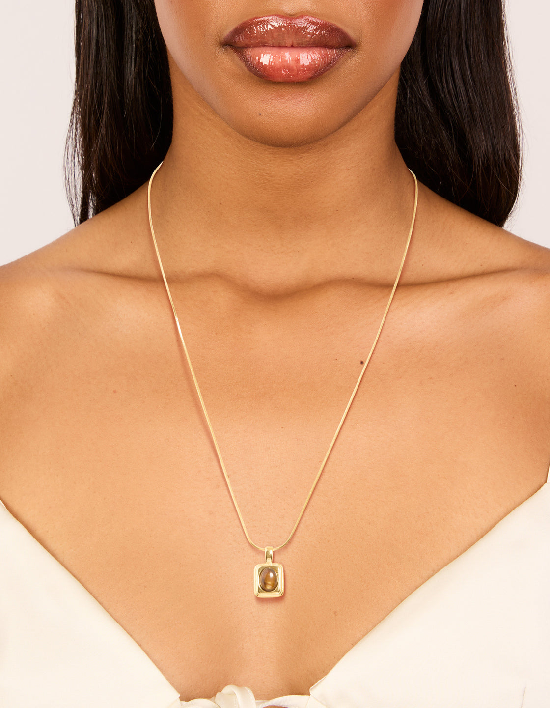 Featuring a waterproof pendant necklace in gold plated stainless steel with tigers eye semi precious stone disc on neck view
