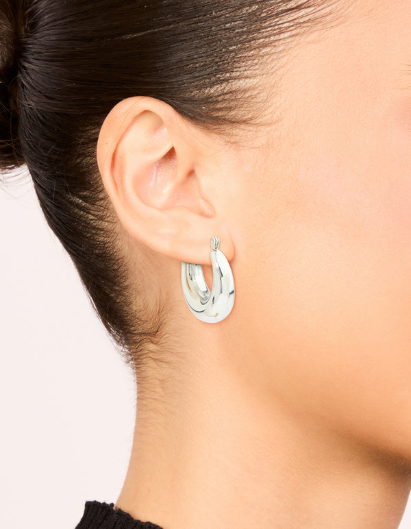 Featuring waterproof stainless steel small chunky huggie earrings with closure in silver on ear view