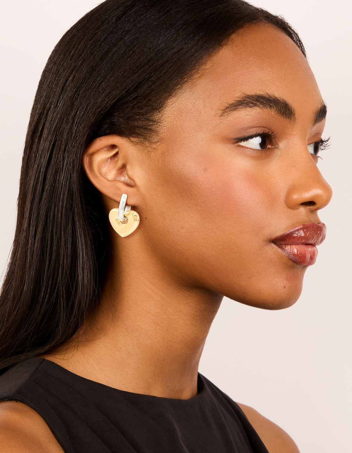 Designed with waterproof mixed metal plated small heart huggie earrings in stainless steel with gold and silver tones on model view