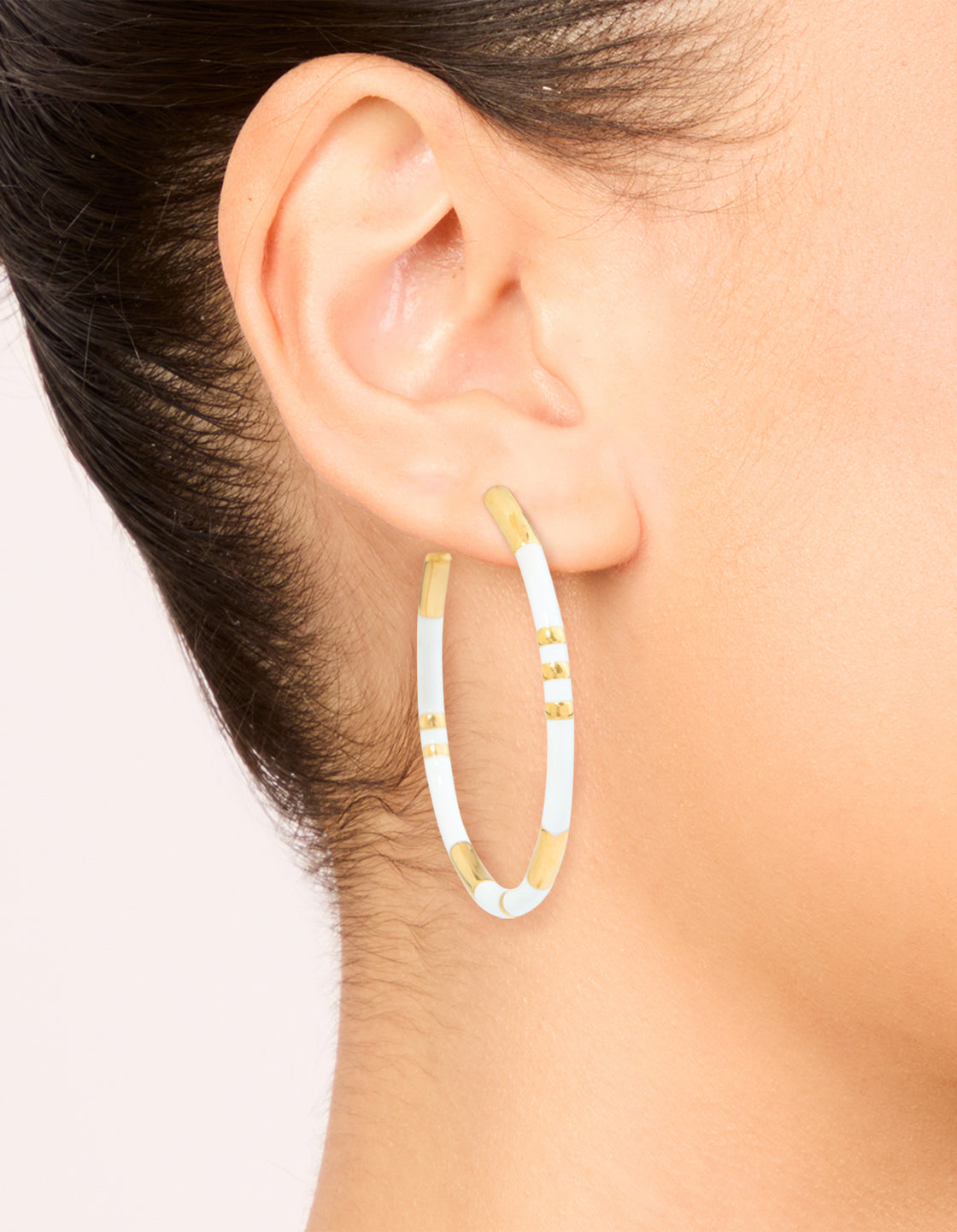 Elegant waterproof statement hoop earrings in stainless steel featuring white enamel and gold plated accents on ear view