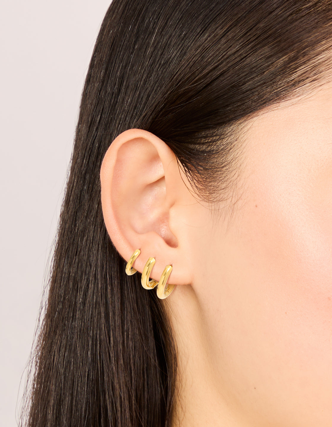 Featuring small huggie earrings in a 3-pack, made with waterproof gold plated stainless steel on ear view