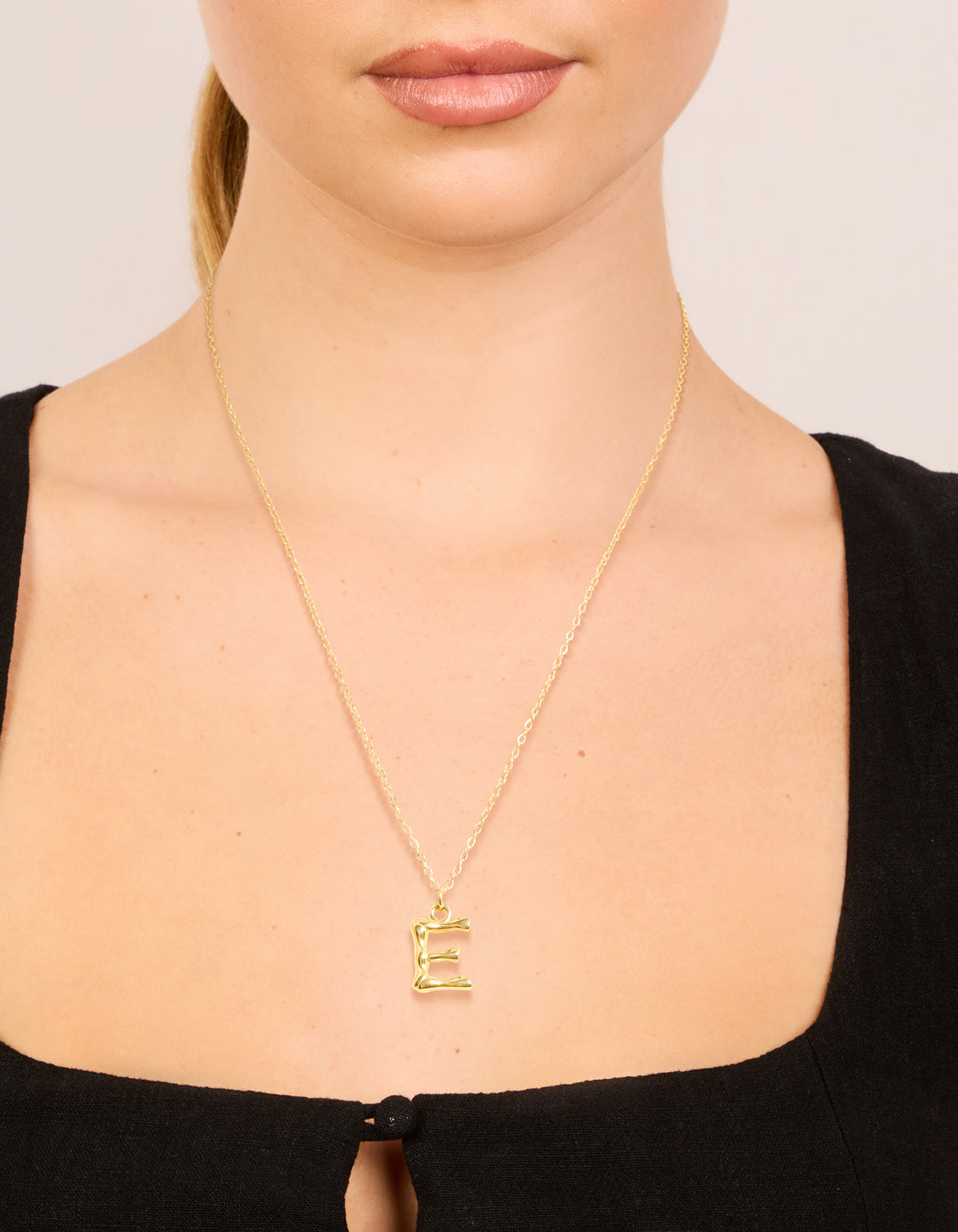 This waterproof gold plated stainless steel bamboo letter E initial pendant necklace is shown in a dainty style on neck view