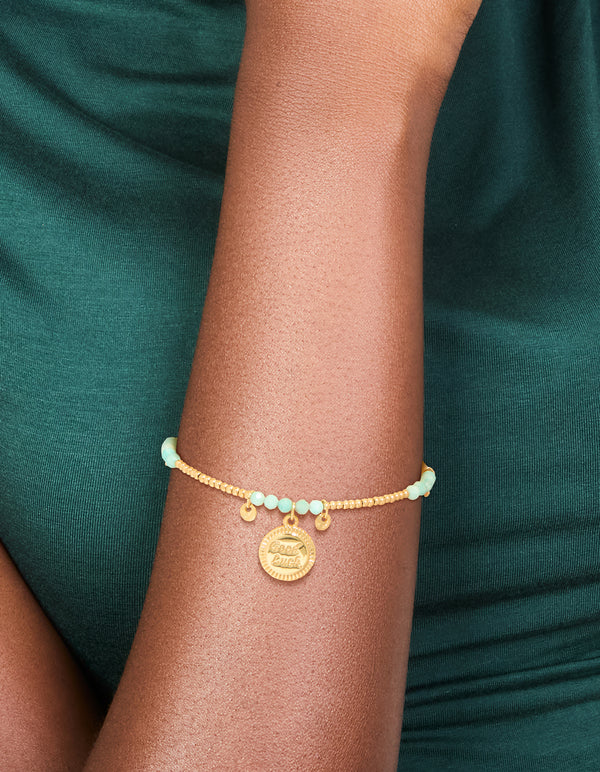 Showcasing a waterproof beaded bracelet crafted from gold plated stainless steel, featuring aquamarine beads and script charms in a dainty style on wrist view