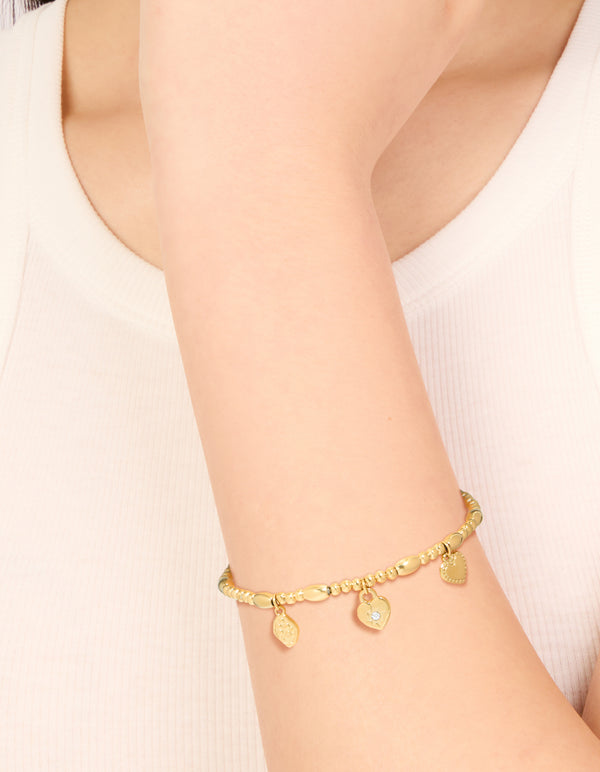 Showcasing a waterproof gold-plated stainless steel stretch bracelet featuring a triple heart, beaded, padlock, and charm design on wrist view
