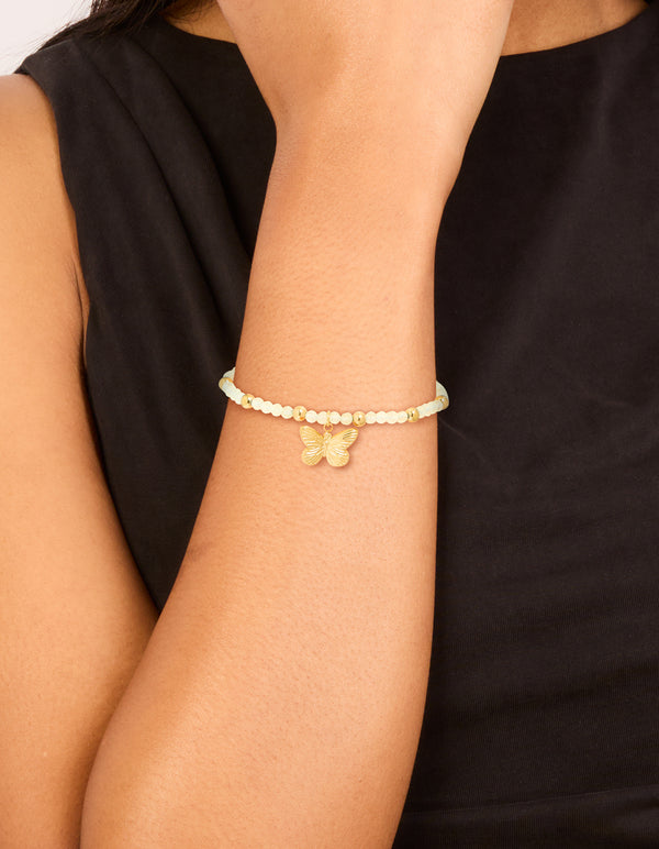 Showcasing a waterproof gold plated stainless steel green semi precious stone butterfly stretch bracelet with beads on wrist view