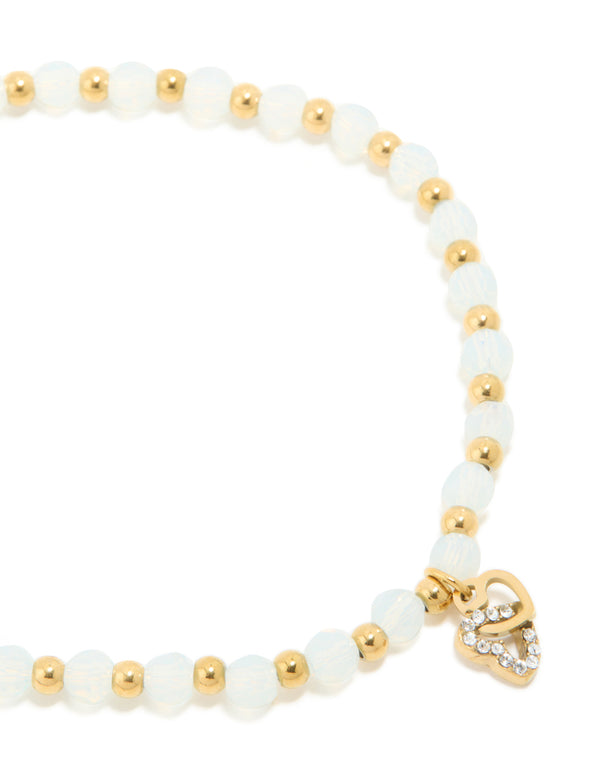 Showcasing a waterproof gold plated stainless steel beaded stretch bracelet with clear quartz stones and dainty heart charm close up view