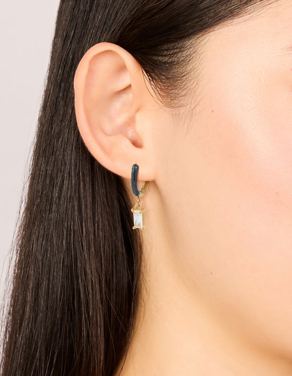 Showcasing waterproof gold plated stainless steel black enamel cubic zirconia huggie earrings with charm in a statement style on ear view