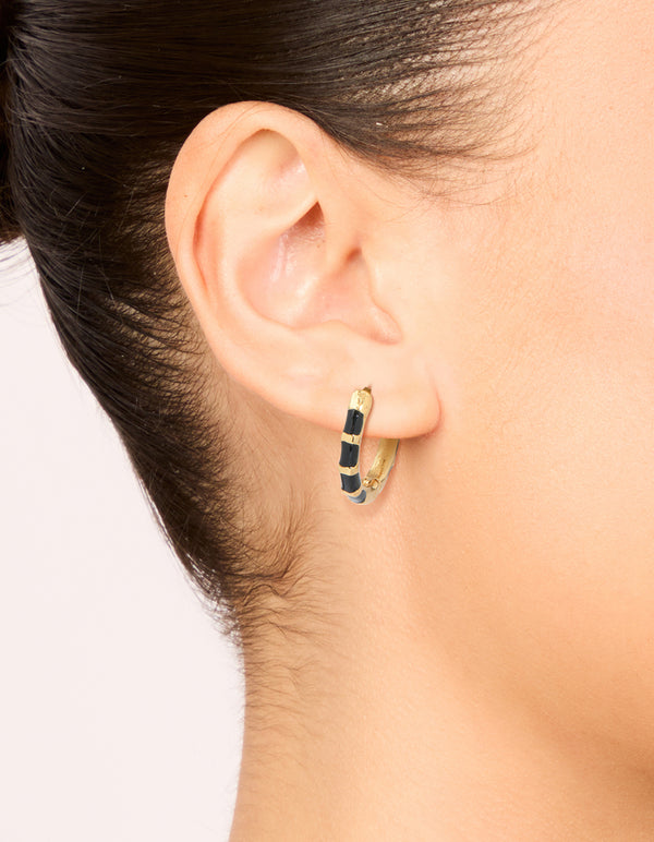 Showcasing waterproof stainless steel huggie earrings with bamboo-inspired segments in gold and black enamel on ear view