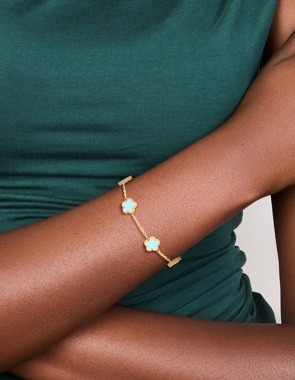 Featuring a waterproof gold plated stainless steel light blue petal flower charm bracelet in powder blue and gold on wrist view
