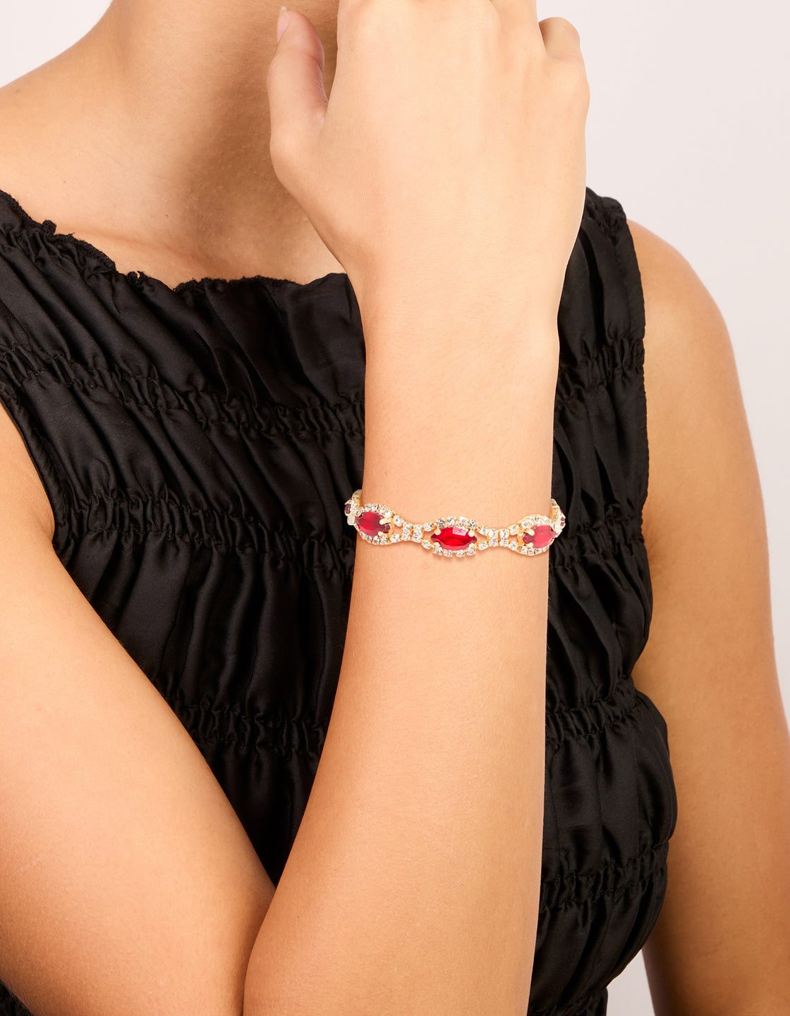Showcasing a gold bracelet featuring red pear shape diamante stones with clear crystal accents on wrist view