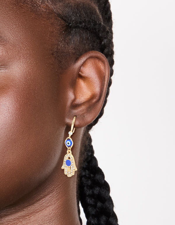 Showcasing gold cubic zirconia evil eye and hamsa hand drop earrings with charm and royal blue detailing on ear view