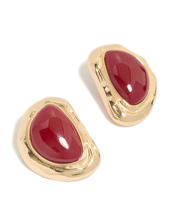 Showcasing statement stud earrings with organic textured design featuring dark red stone in gold finish front view