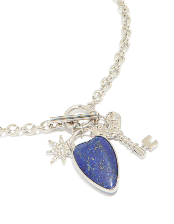 Showcasing a silver diamante and blue stone heart chunky style necklace with celestial charms featuring star pendant close up view