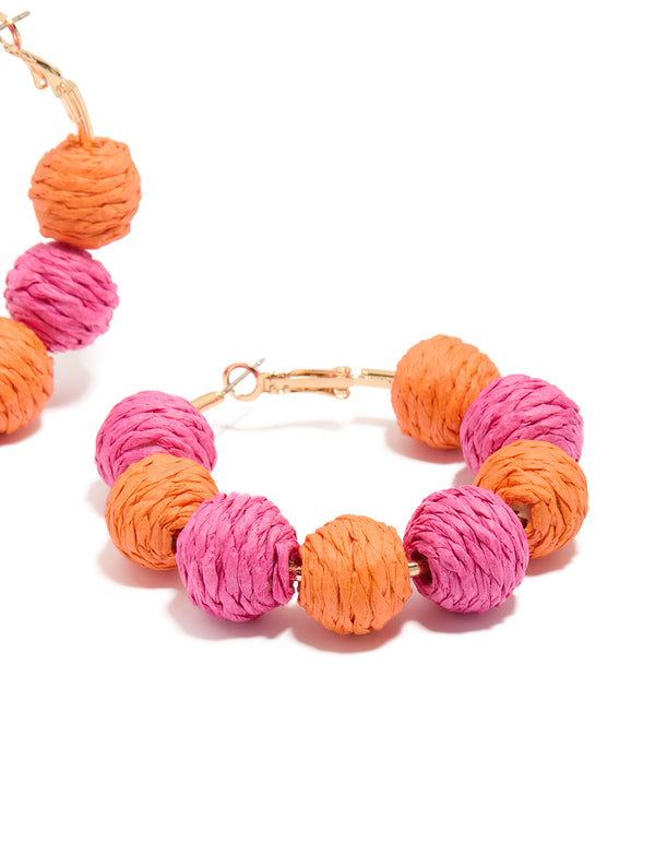 Featuring statement hoop earrings with alternating light pink and coral paper-wrapped balls post detail view