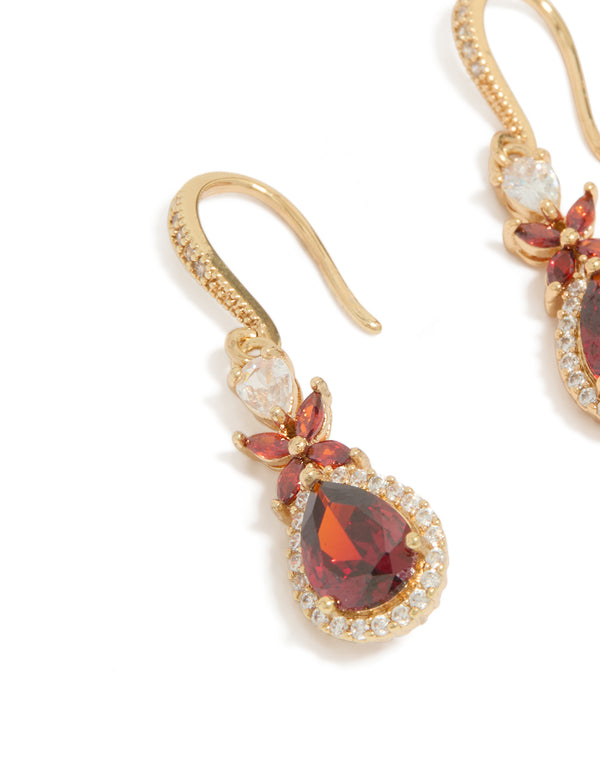 A detailed look at the intricate stone arrangement and metal texture on these statement drop earrings featuring dark red teardrop cubic zirconia with clear accents in gold, close up view