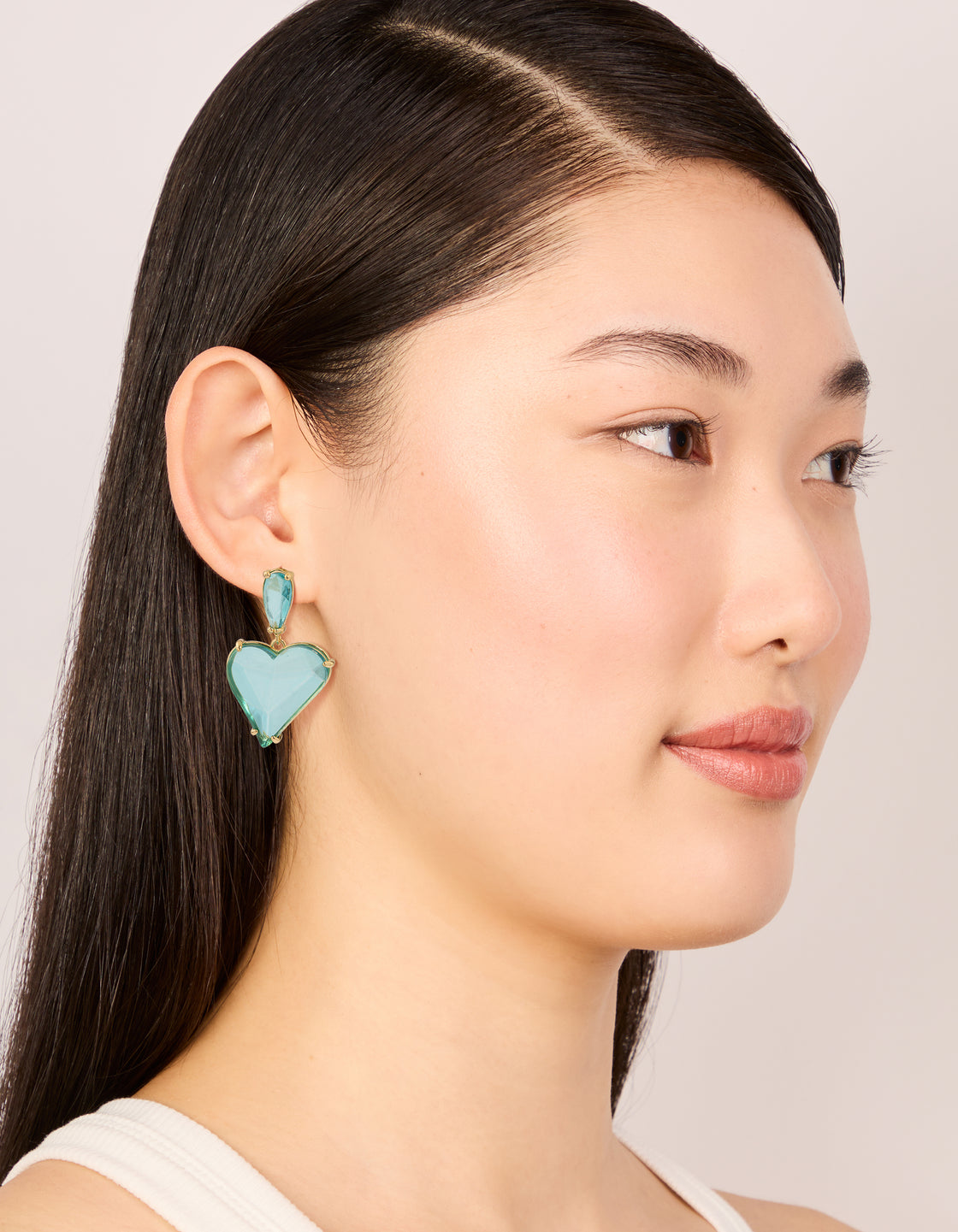 Featuring statement drop earrings with heart design in blue glass stone and gold finish on model view