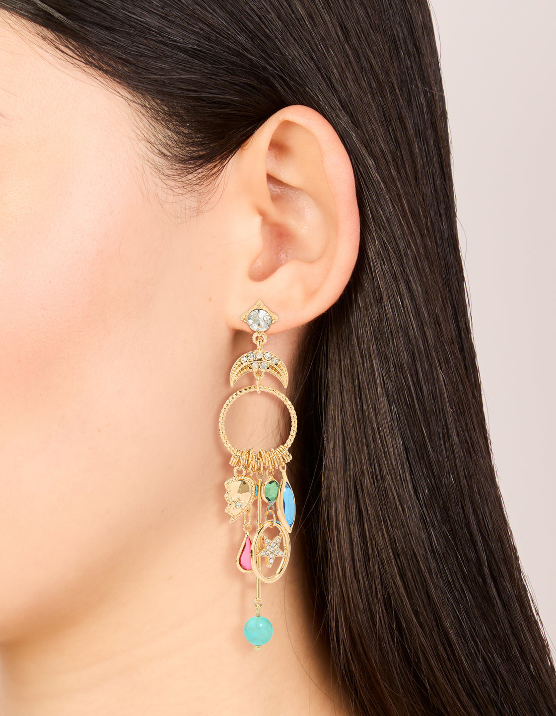 Featuring statement gold moon and circle charm drop earrings with evil-eye, celestial design, star details, beads in turquoise, pink, and green on ear view