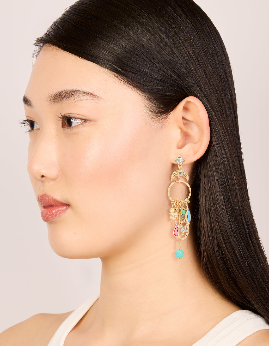 Designed with statement style, gold moon and circle charm drop earrings featuring evil-eye, celestial motifs, star accents, beads in turquoise, pink, and green on model view
