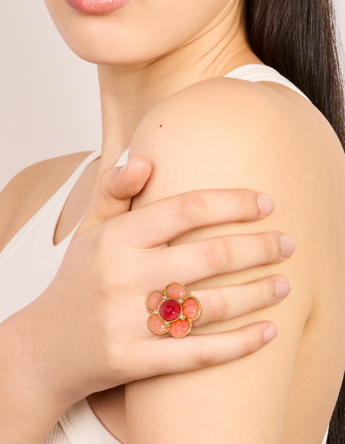 Showcasing a statement pink stone flower ring in gold plated metal with light coral crimson accents on finger view