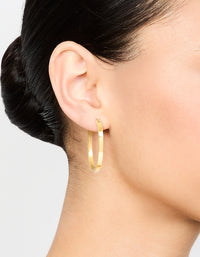 Featuring waterproof medium flat hoop earrings in gold plated stainless steel worn on ear view - link has visual effect only