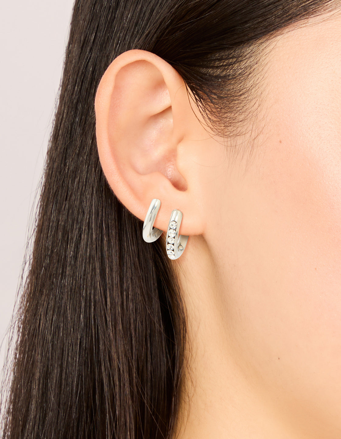Showcasing waterproof stainless steel cubic zirconia and smooth chunky huggie earrings in a 2-pack with crystal accents on ear view
