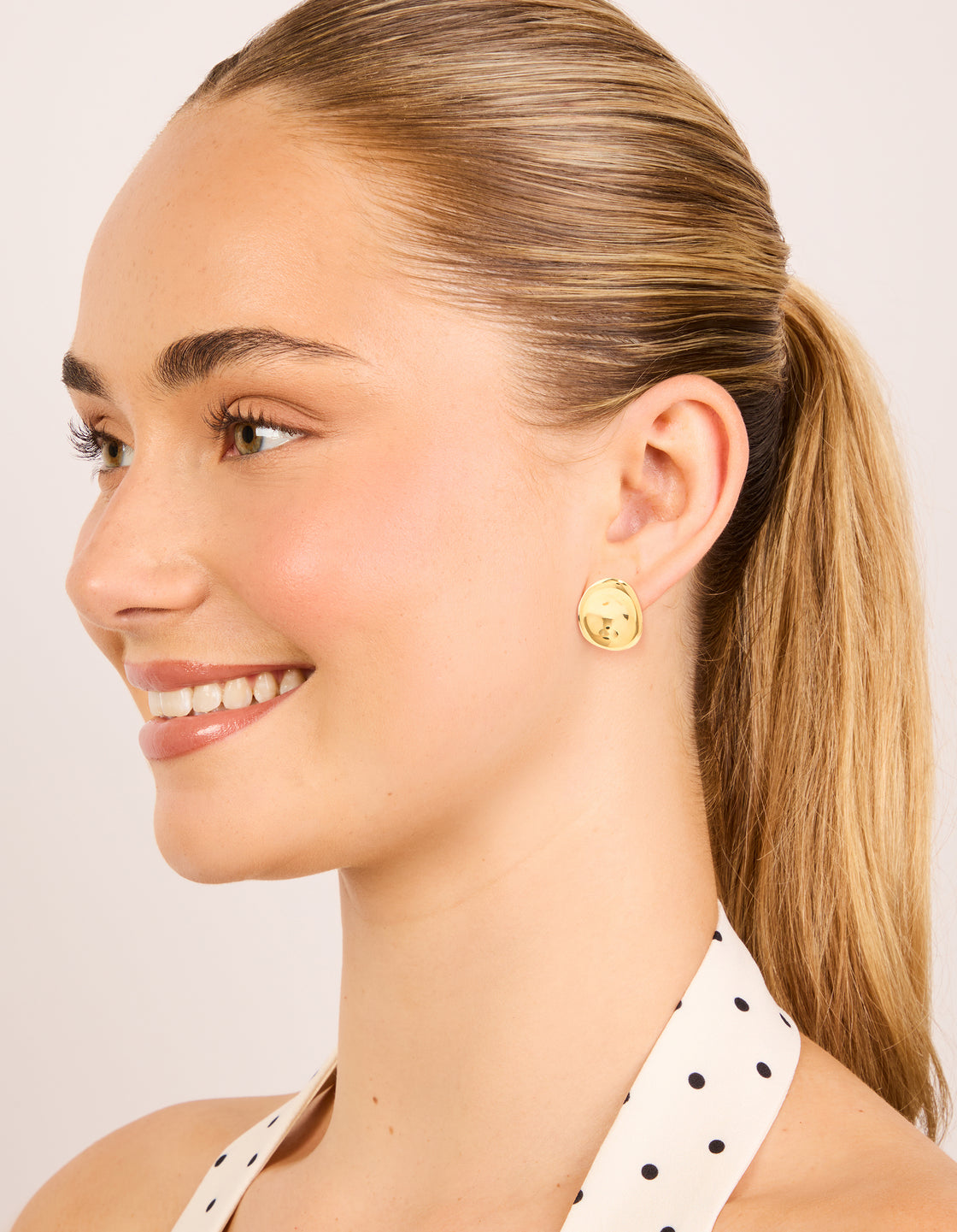 Showcasing waterproof gold plated stainless steel button stud earrings in gold with stud closure on model view
