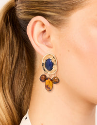 Showcasing statement charm and beaded medallion drop earrings in gold with midnight blue acrylic and saddle brown accents on ear view - link has visual effect only
