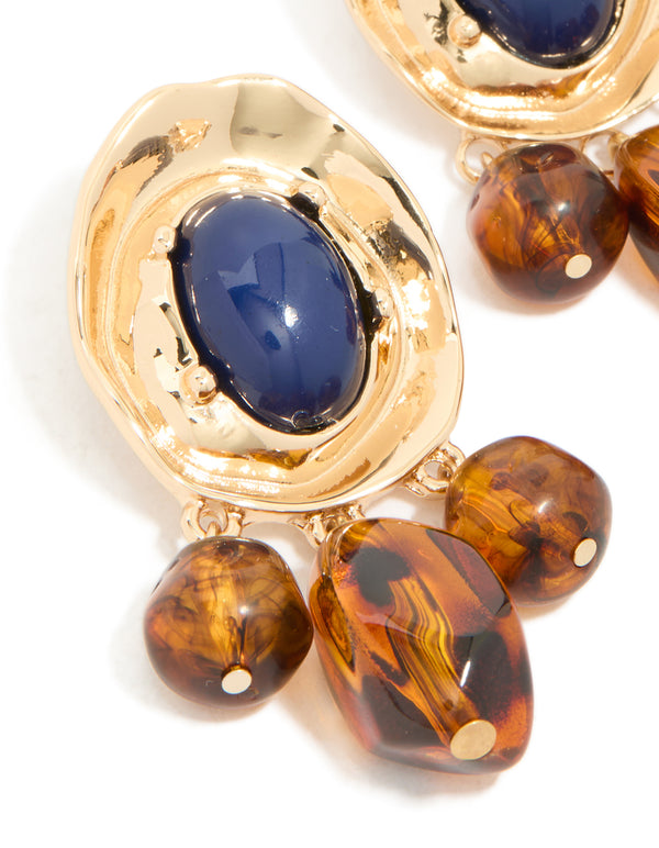 Highlighting statement charm and beaded medallion drop earrings in gold with midnight blue acrylic and saddle brown details close up view