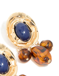 Highlighting statement charm and beaded medallion drop earrings in gold with midnight blue acrylic and saddle brown details close up view - link has visual effect only