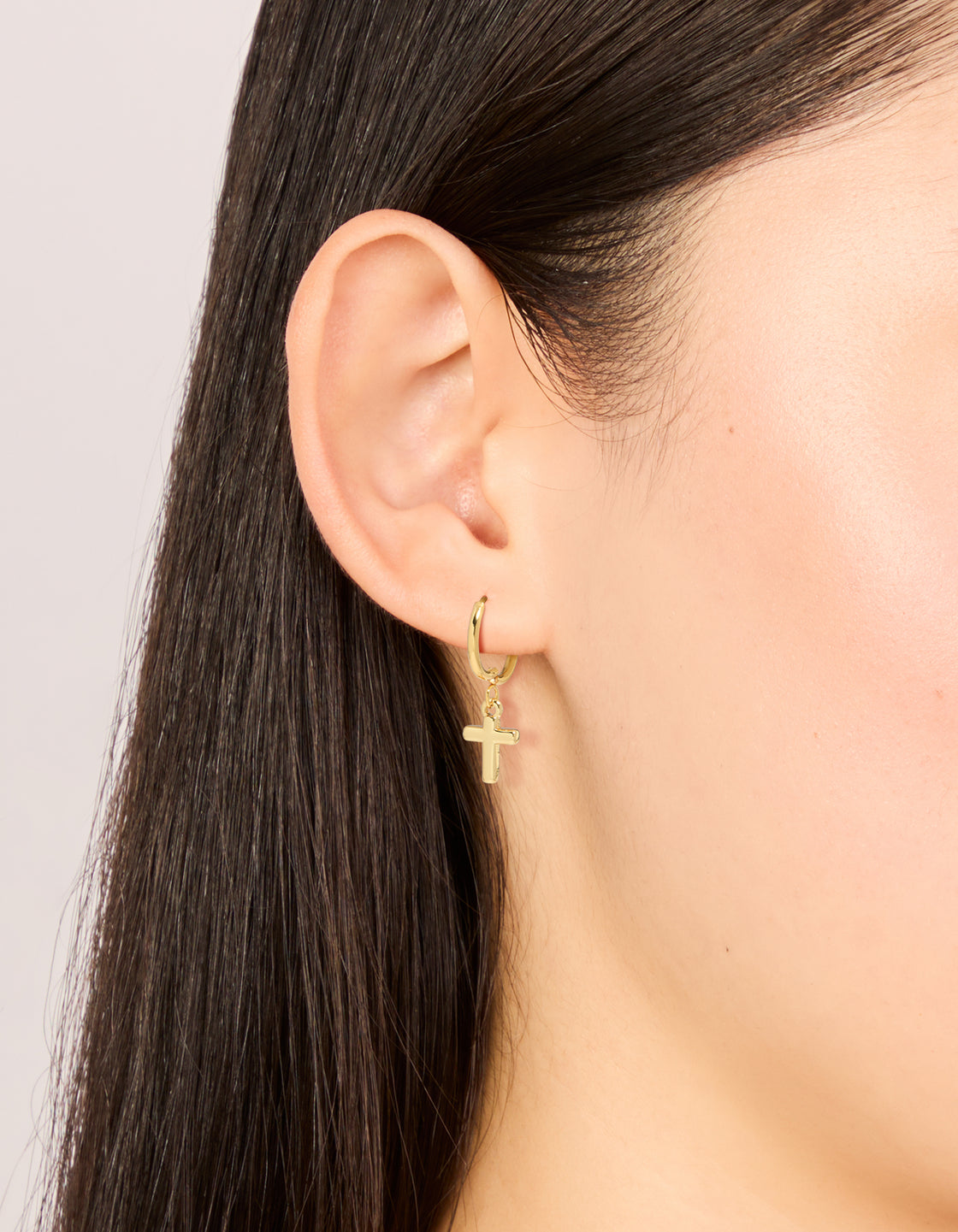 Showcasing waterproof gold plated stainless steel cross huggie earrings on ear view