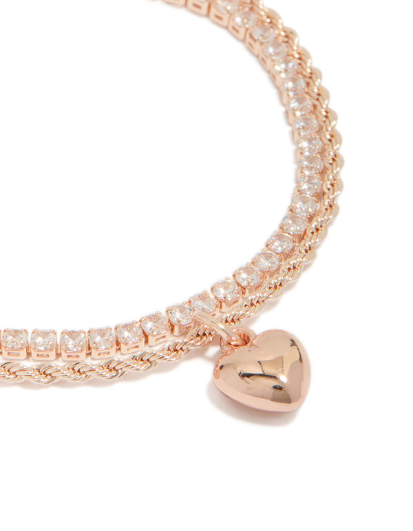 Highlighting a rose gold plated cubic zirconia tennis and heart layered bracelet with charm detail close up view