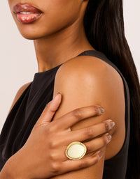 Crafted from gold plated material, this oval cream stone ring features statement design on finger view - link has visual effect only