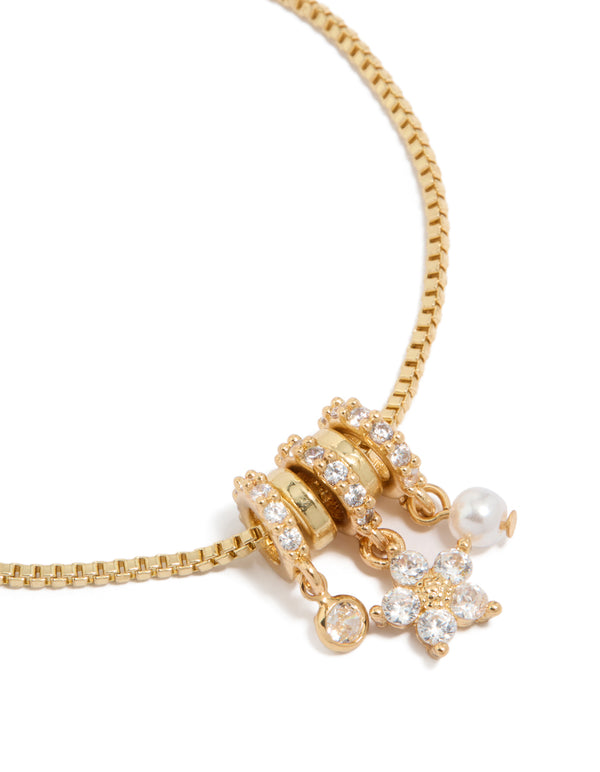 Featuring a gold plated bracelet with cubic zirconia flower and pearl rondell charm accents in a toggle design close up view