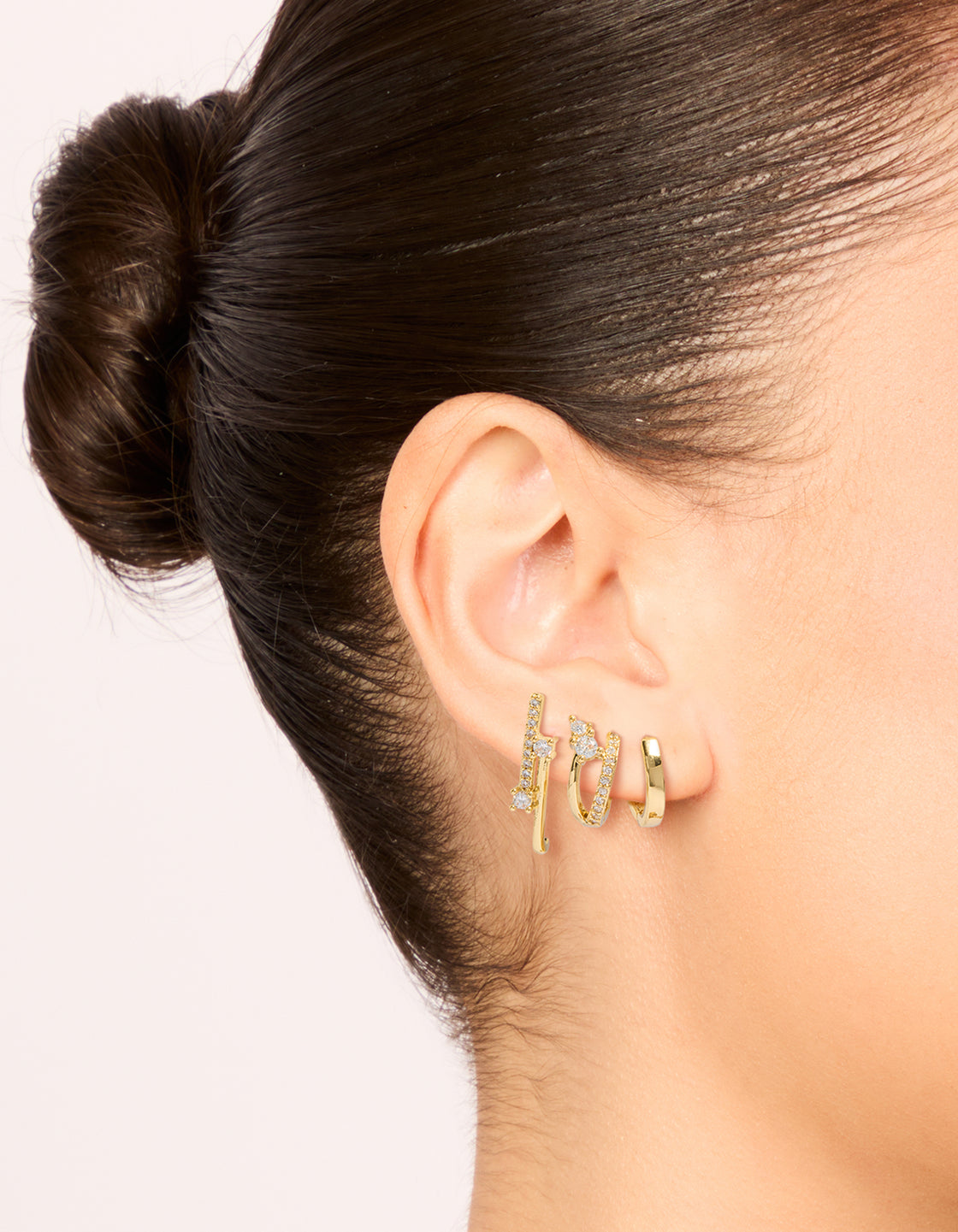 Showcasing gold plated cubic zirconia studs and double cuff huggie earrings in a 3-pack, crystal accents, and clear color tones on ear view