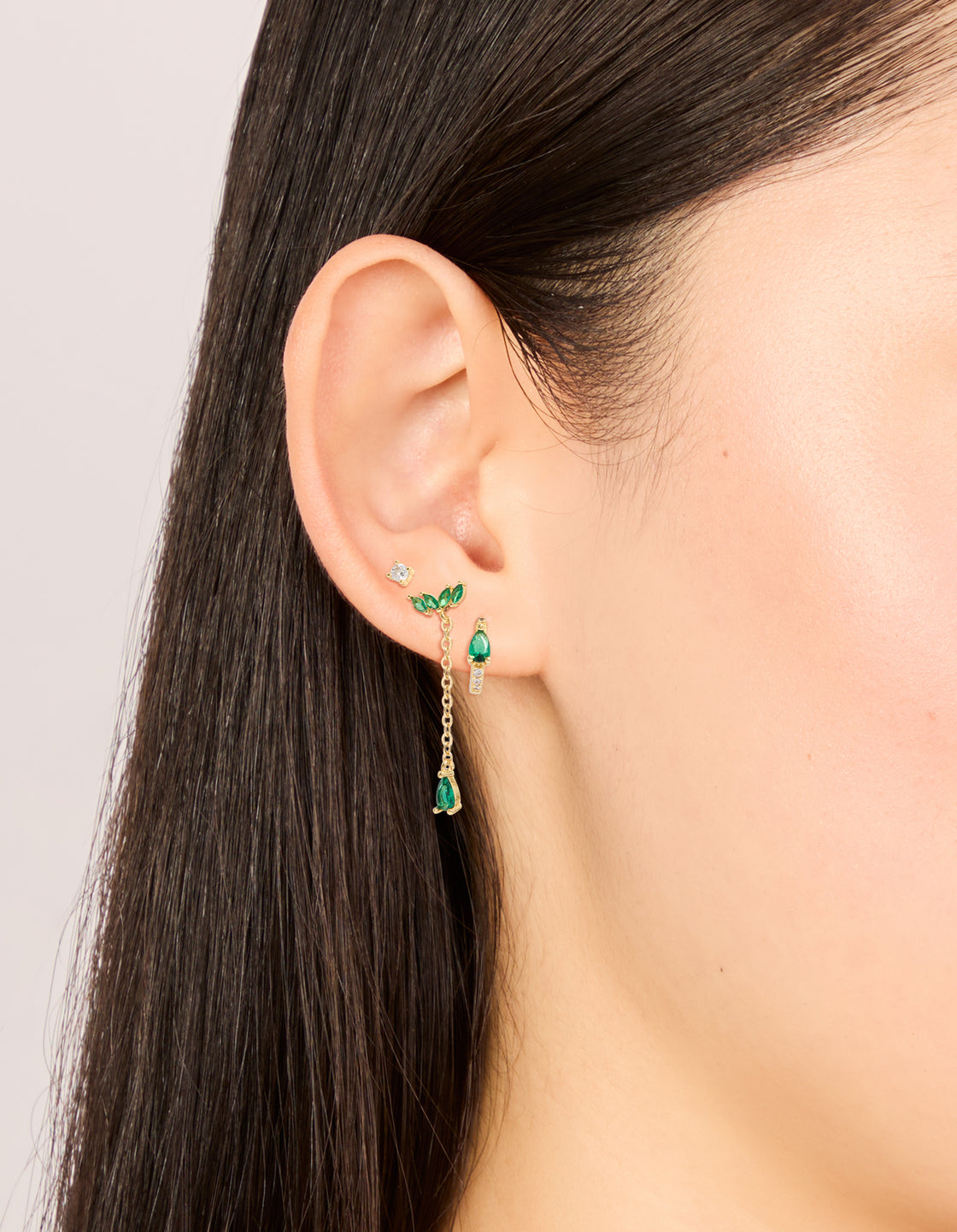 Crafted from gold plated clear and green cubic zirconia pear chain and stud earrings 3-pack with statement featuring marquise, oval stone cut crystal star accents, hoop and stud closures in white on ear view