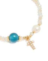 Designed with gold plated metal, this dainty beaded bracelet features a cross charm with cubic zirconia, freshwater pearl accents, and turquoise beige white details close up view - link has visual effect only