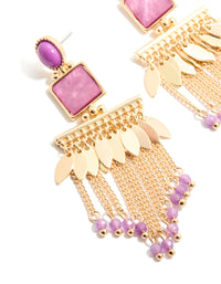 Highlighting statement drop earrings in gold with purple oval stones, leaf charms and beaded chain tassels in close up view - link has visual effect only