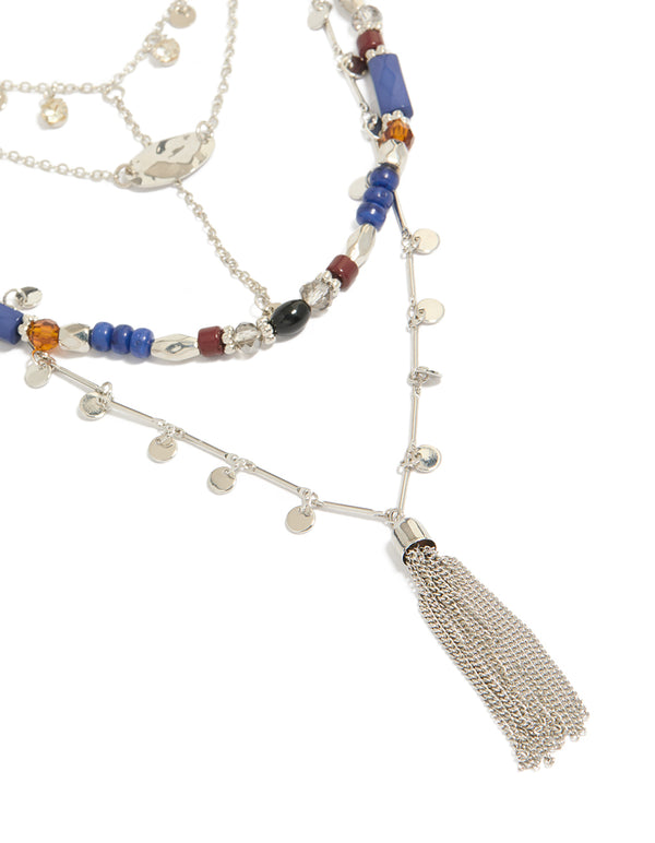 Showcasing a blue and brown beaded layered necklace featuring a tassel, charm disc, cubic zirconia, and crystal accents in silver, close up view