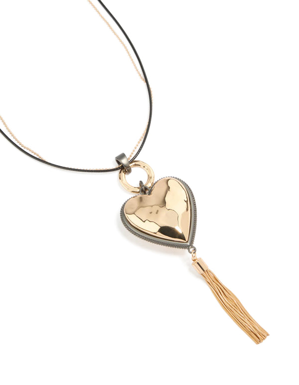 Showcasing a mixed metal chunky heart tassel cord layered necklace featuring charm details in silver and gold close up view
