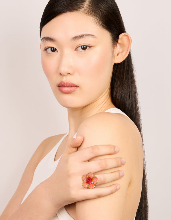 Elegant statement flower ring with gold plated material featuring pink stone in coral, crimson, and clear on finger view