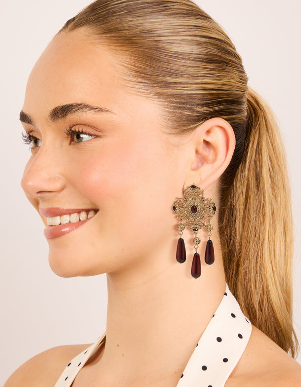 Crafted from gold with charm, and beads design statement drop earrings in maroon on model view