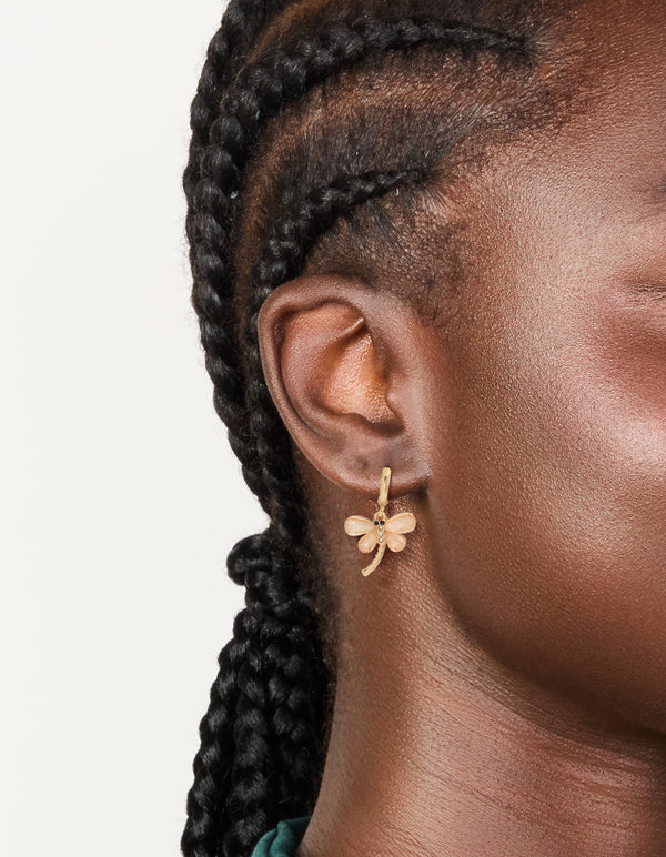 Featuring pink dragonfly gold huggie hoop earrings with animal charm, wings, and glitter accents on ear view