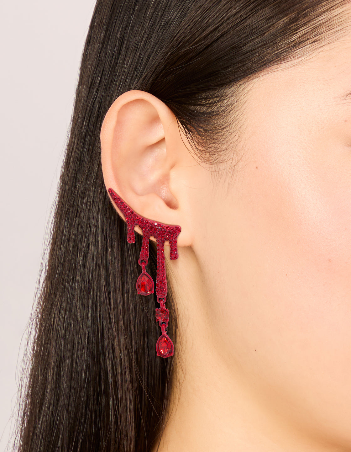 Displaying statement red coated metal blood droplet drop earrings with charm featuring and glitter in crimson on ear view