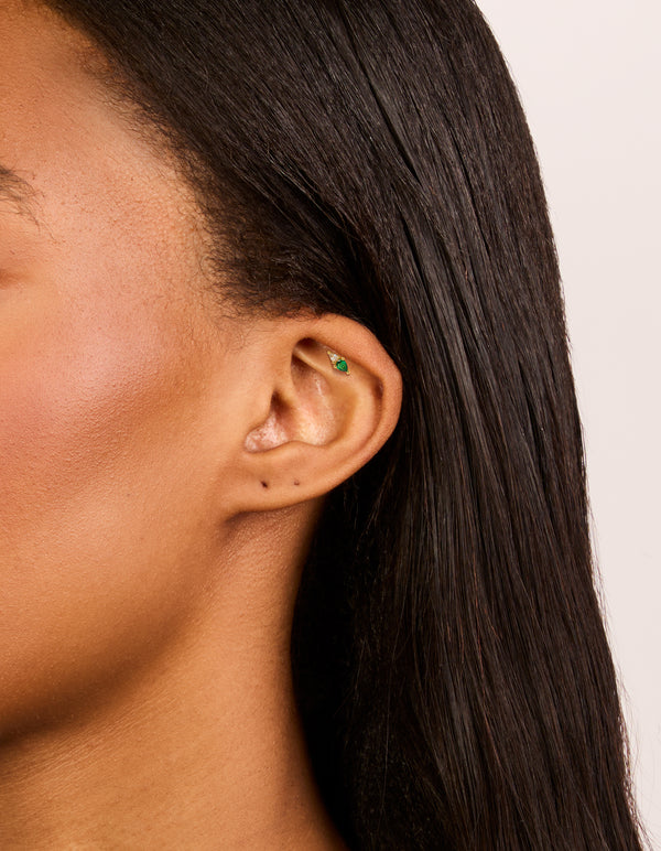 Featuring a dainty stud earring crafted from gold plated surgical steel with green and clear cubic zirconia crystals and flat back closure on ear view